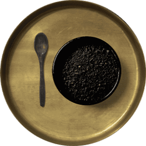 A bowl of black tea with a spoon on a gold plate.